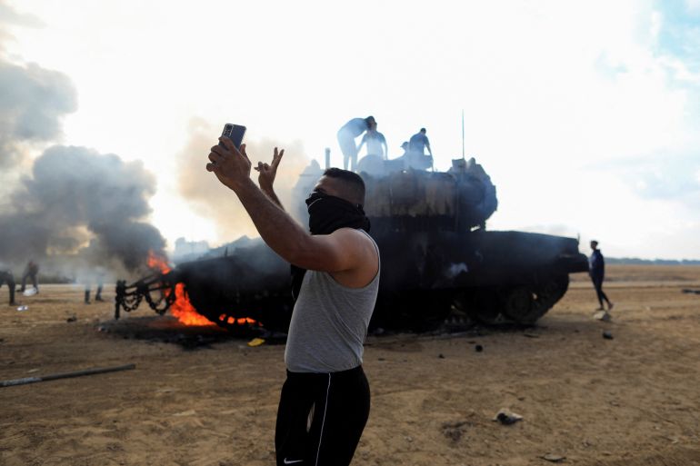 A Palestinian man takes a selfie in front of a burning Israeli military vehicle after it was hit by Palestinian gunmen who infiltrated areas of southern Israel, at the Israeli side of Israel-Gaza border, October 7, 2023. REUTERS/Yasser Qudih NO RESALES. NO ARCHIVES.