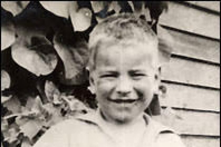 A black and white photo of a 6-year-old boy with blond hair wearing light-colored coveralls.